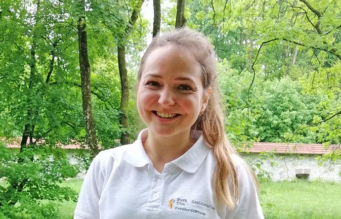 Lächelnde Pflegeauszubildende in weißem Polo vor Bäumen