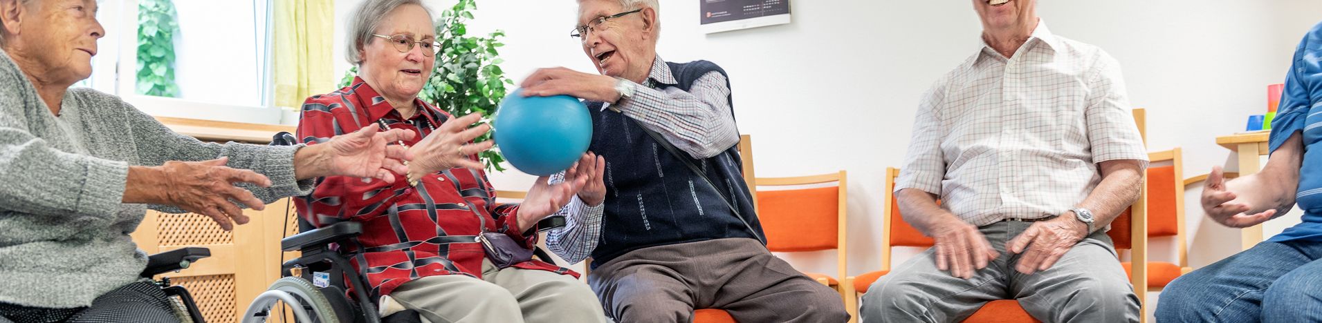 Ältere Menschen im Sitzkreis geben sich einen blauen Ball