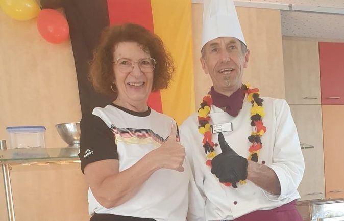 Zwei lächelnde Personen vor deutscher Flagge mit Daumen hoch