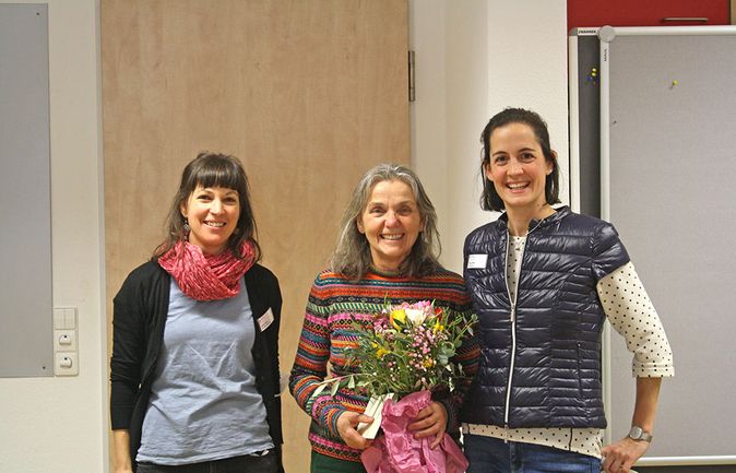 Drei Frauen lächeln bei Verabschiedung in der Mitte mit Blumenstrauß