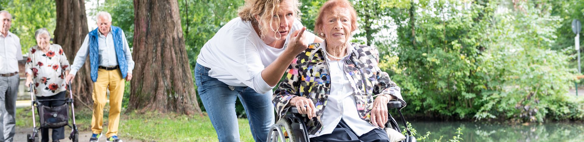 Pflegekraft zeigt der älteren Frau im Rollstuhl etwas im Park