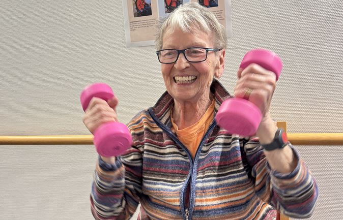 Seniorin hebt pinke Hanteln vor Trimm-mich-Pfad-Poster