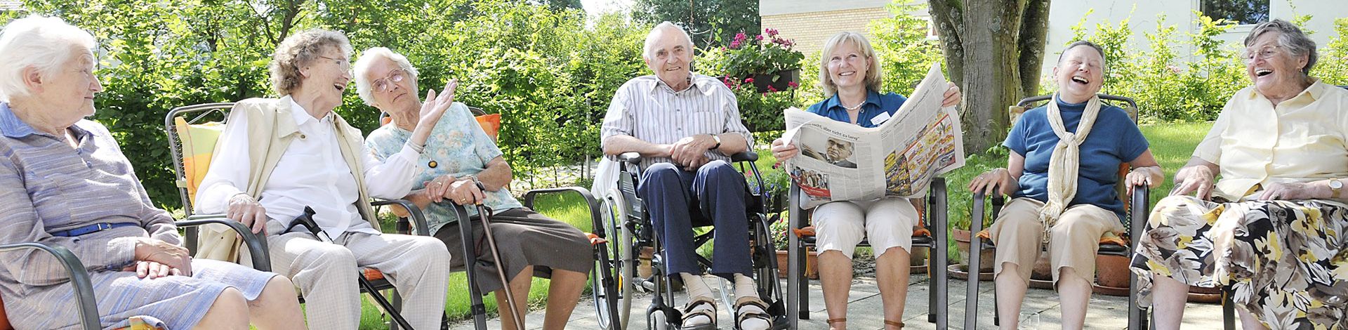 Seniorinnen und Senioren sitzen im Garten lachen teils im Rollstuhl